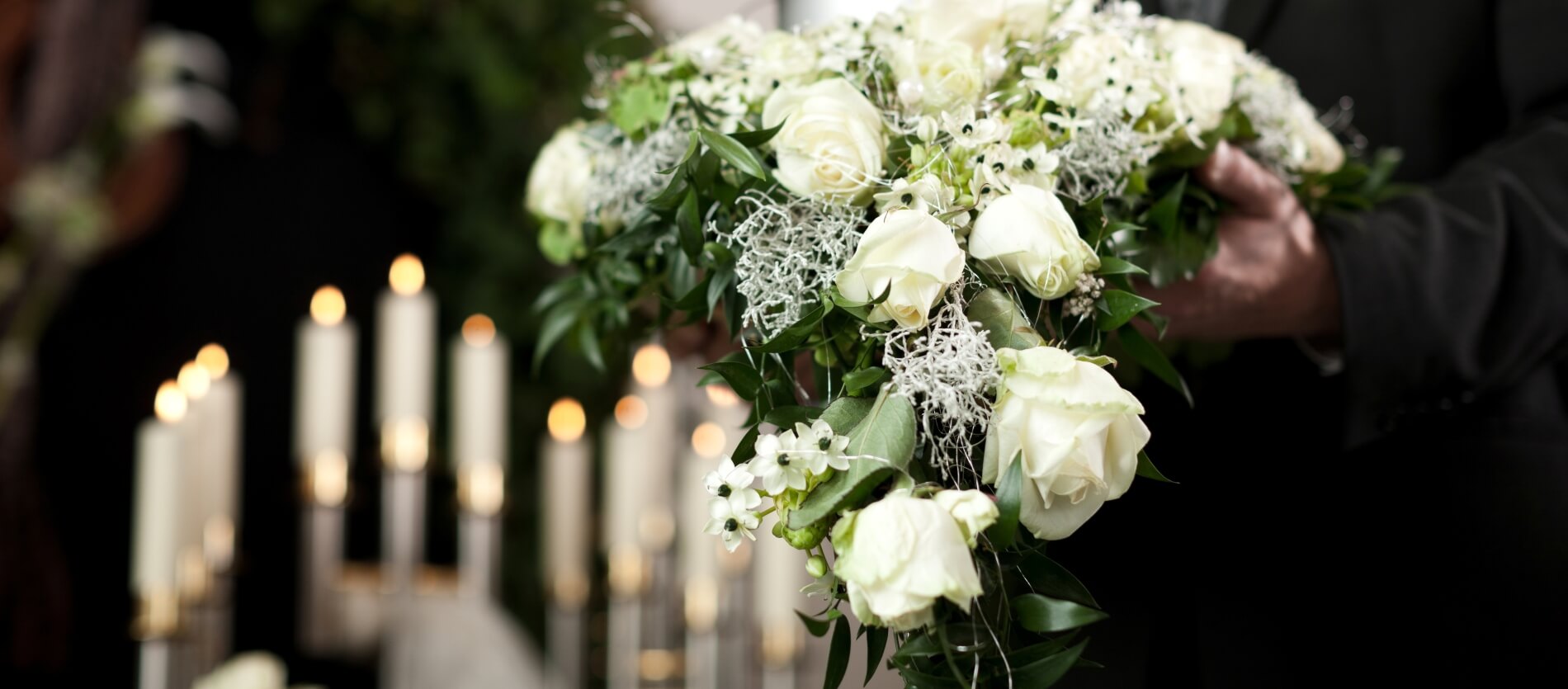 White roses flower arrangement being carried with an urn with candles in the background