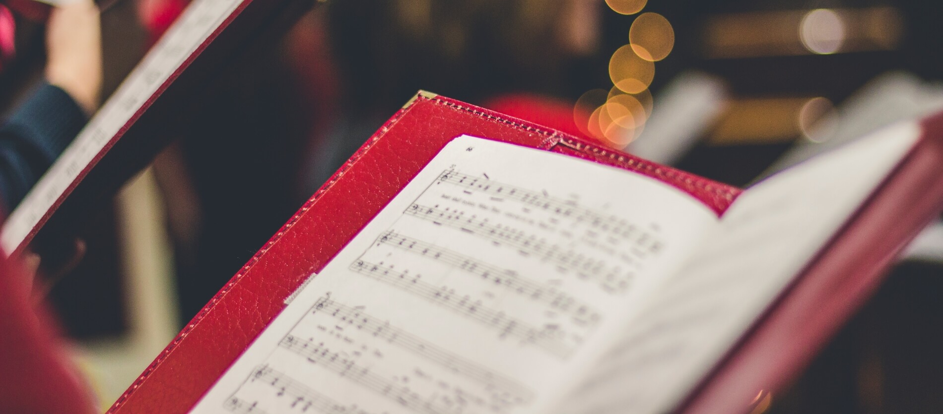 Focused shot of a red song book showing music song sheet. Fairy fairy lights are visible in the background