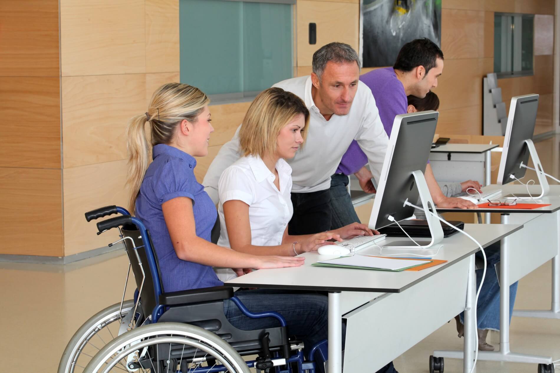 A women in a wheelchair at a desk with two other people looking at a desktop computer