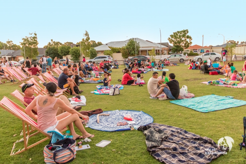 View of grassed area with community members in High Wycombe sitting in deck chairs and blankets getting ready to watch the outdoor movies during the City Summer Series event .