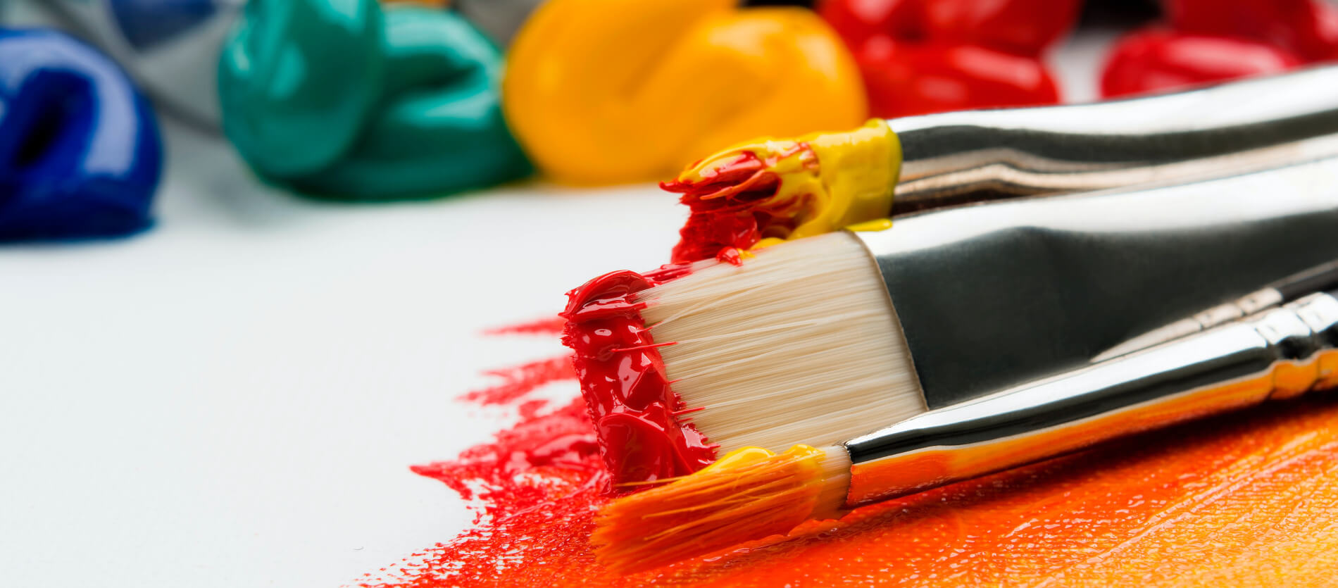 Three paint brushes with reds, yellow and orange colours on the tips of them