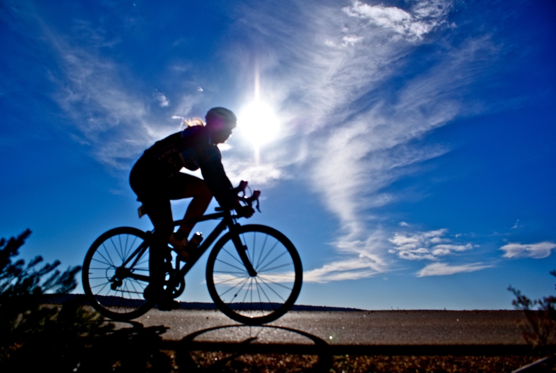 Silhouette of a cyclist riding with sun shining behind him.