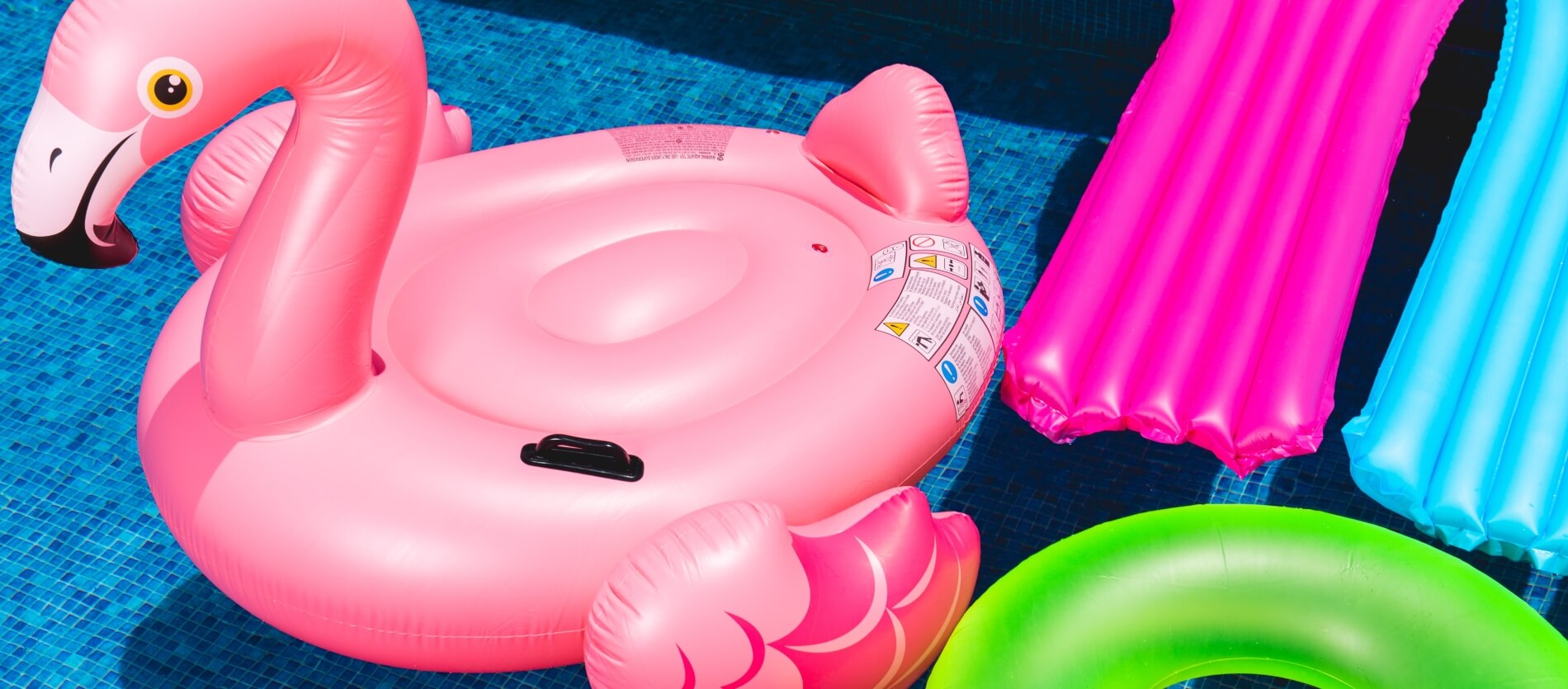 Four inflatable pool accessories including a large pink flamingo, green tube and pink and blue sun loungers